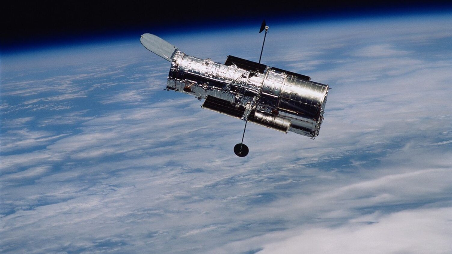 Telescópio espacial Hubble em órbita, com a Terra ao fundo.