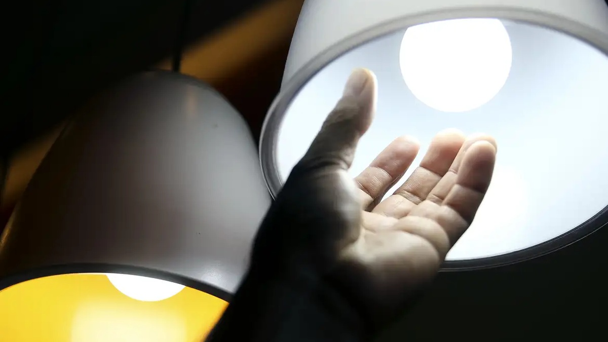 Mão próxima a uma lâmpada acesa em fotografia sobre energia elétrica